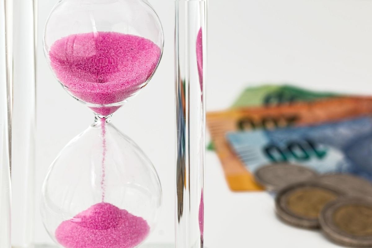 Reloj de arena junto a billetes: el tiempo erosiona el valor del dinero